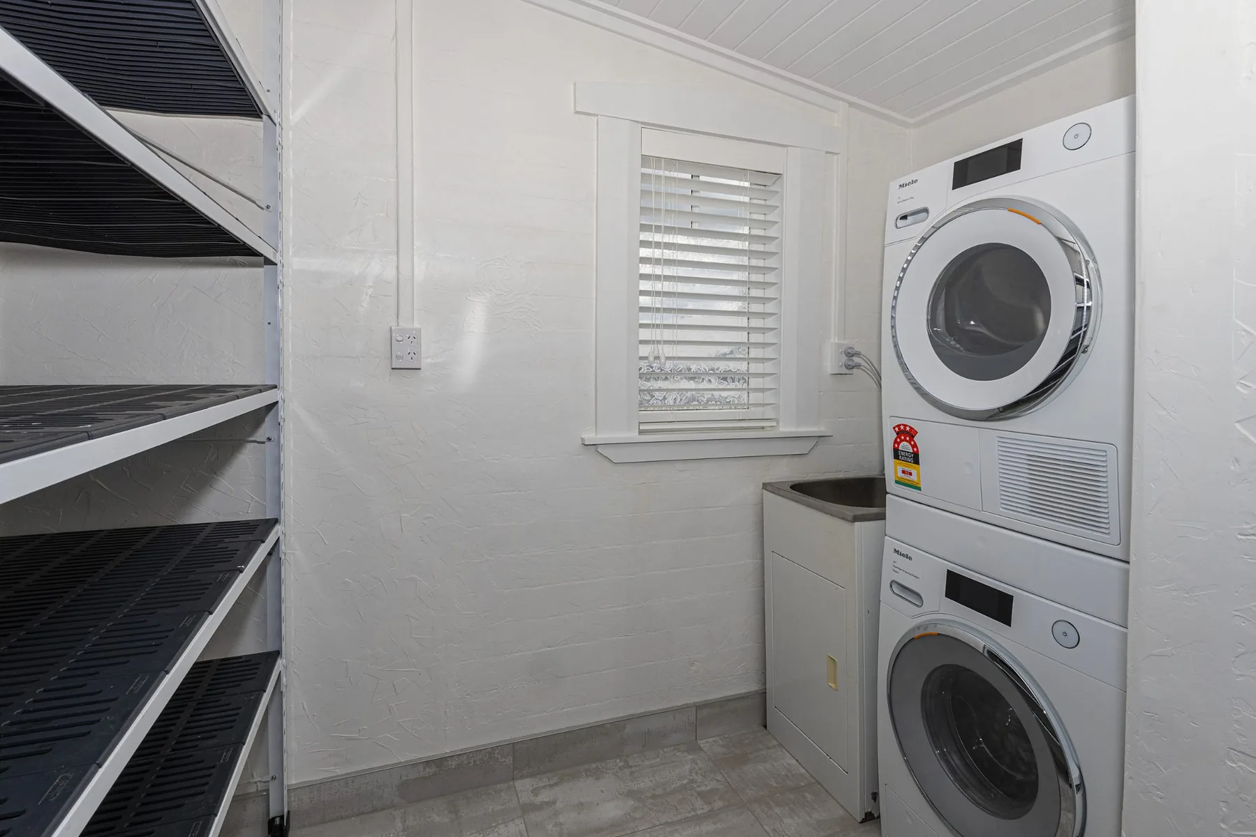 Laundry with stacked appliances, wall storage and white walls