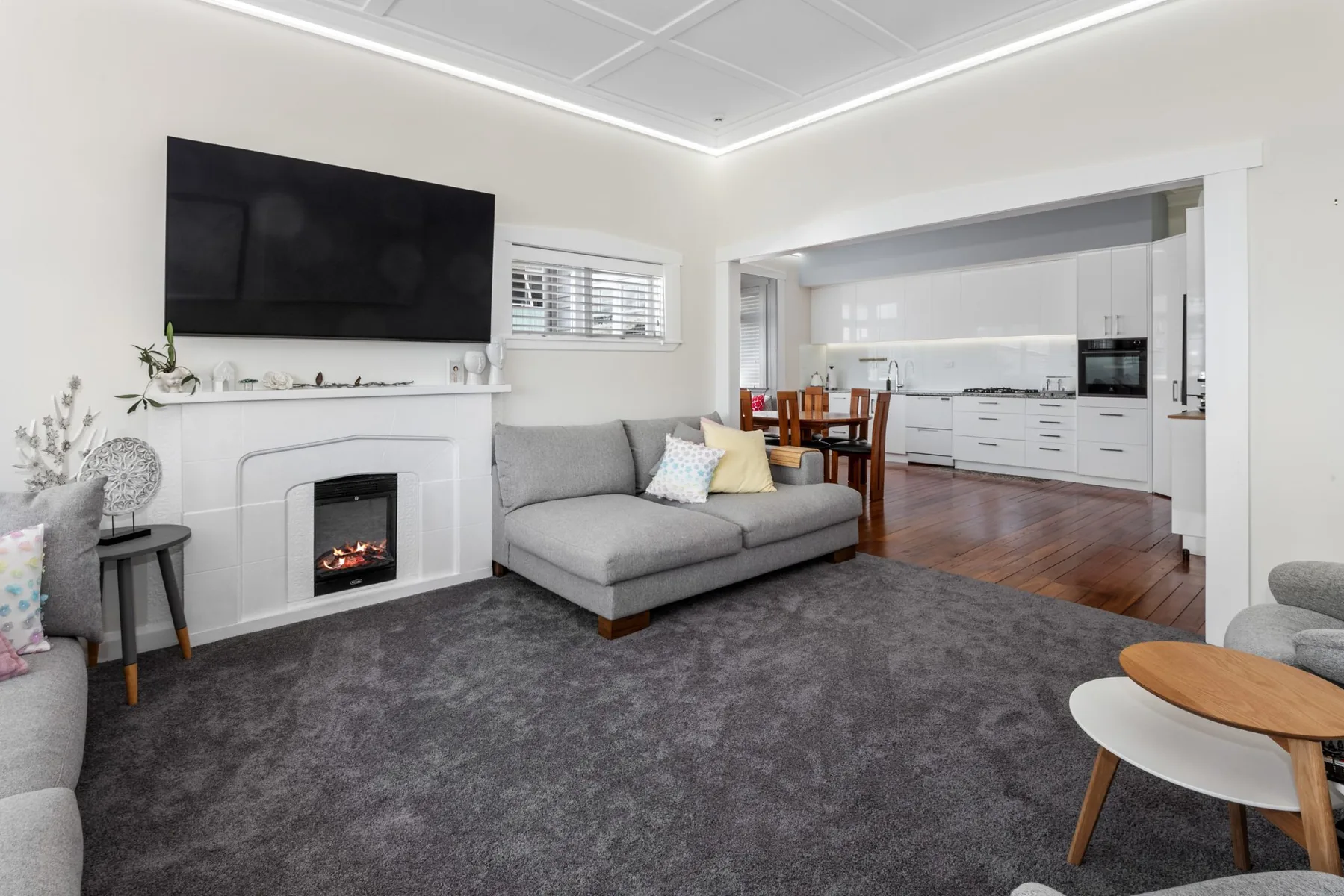 Finished lounge with white walls, grey carpet, fireplace and view towards the kitchen